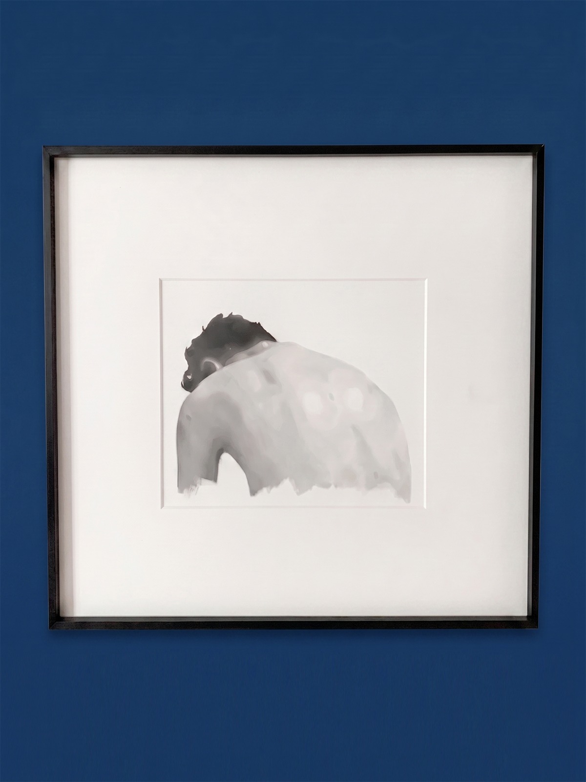 A monochromatic study of a seated figure viewed from behind.
