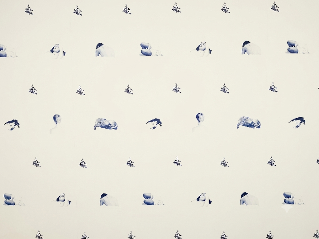 Wallpaper installation composed of repeated monochromatic figures and small floral motifs on a pale wall.