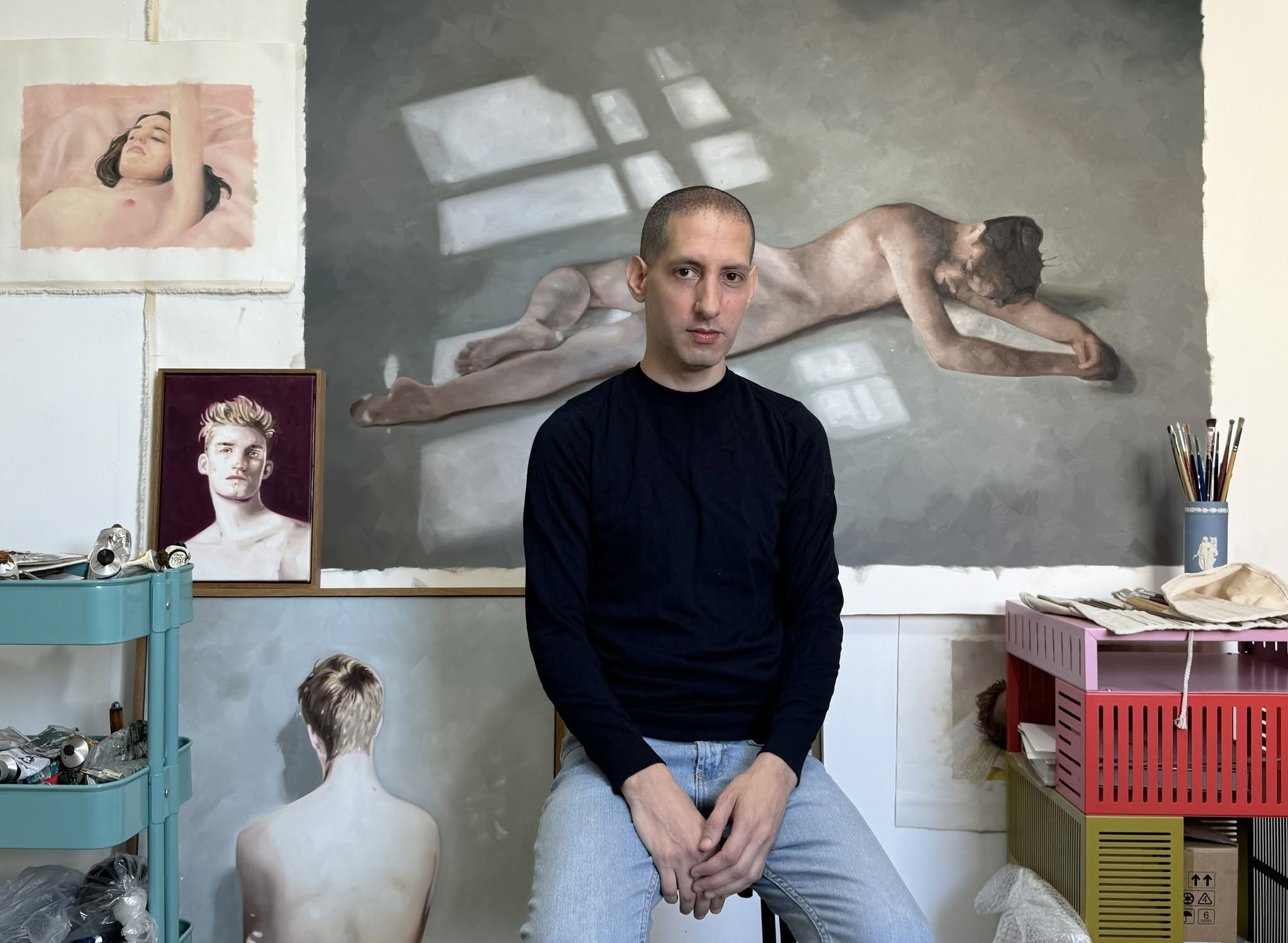 Refael Salem seated in his studio, surrounded by paintings and artists’ materials.