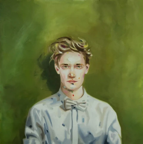 Young man in a light buttoned shirt and bow tie seated against a green background.