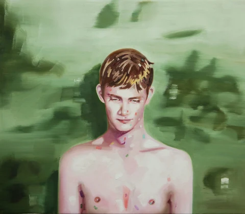 Bare-chested young man standing against a blurred green landscape.