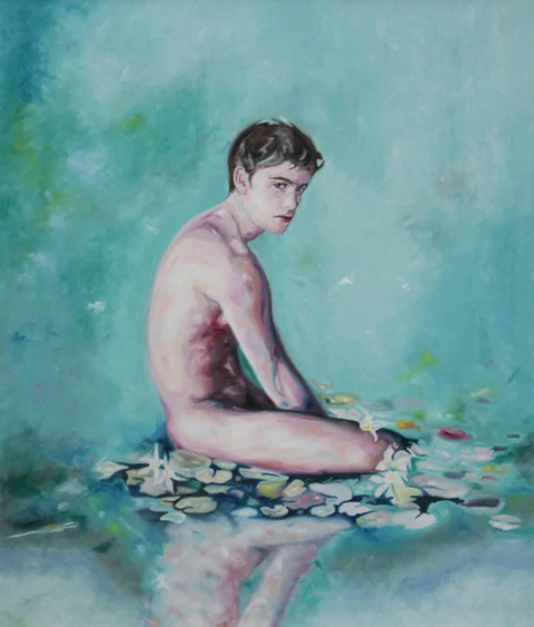 Bare-chested young man seated in shallow water against a turquoise background.
