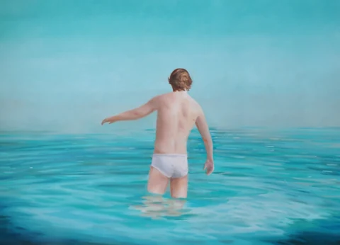 Figure walking into calm turquoise water beneath a clear sky.