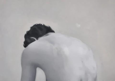 Black-and-white view of a seated figure bent forward, shown from behind.