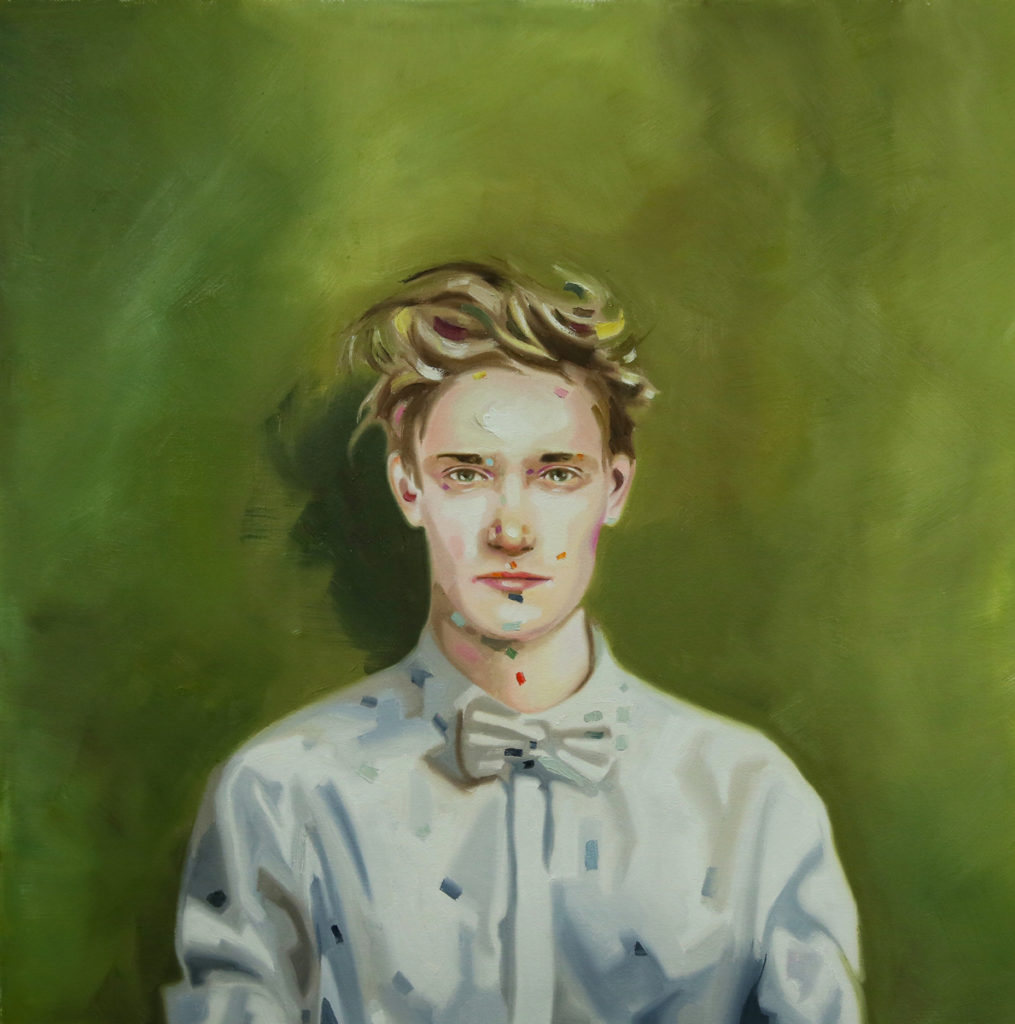Young man in a light buttoned shirt and bow tie seated against a green background.