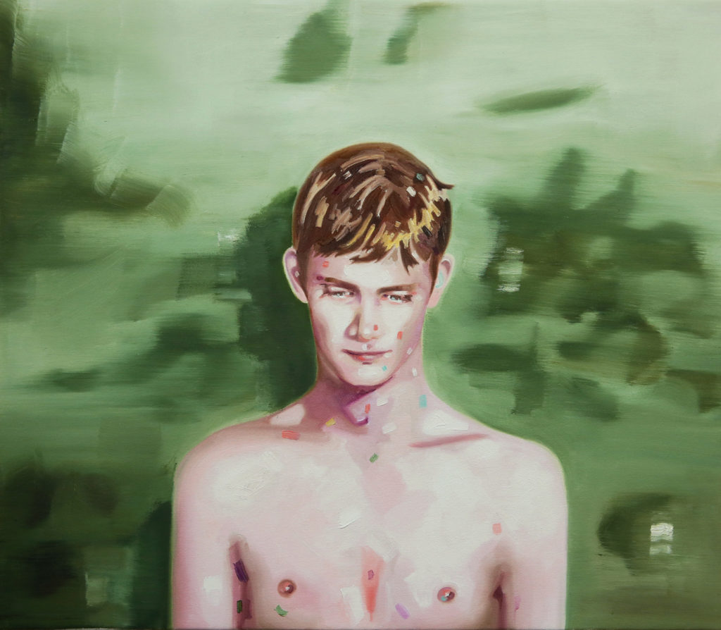 Bare-chested young man standing against a blurred green landscape.