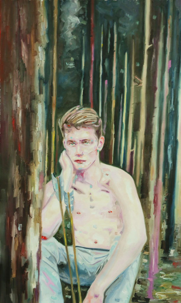 Bare-chested young man standing among dark vertical tree trunks.