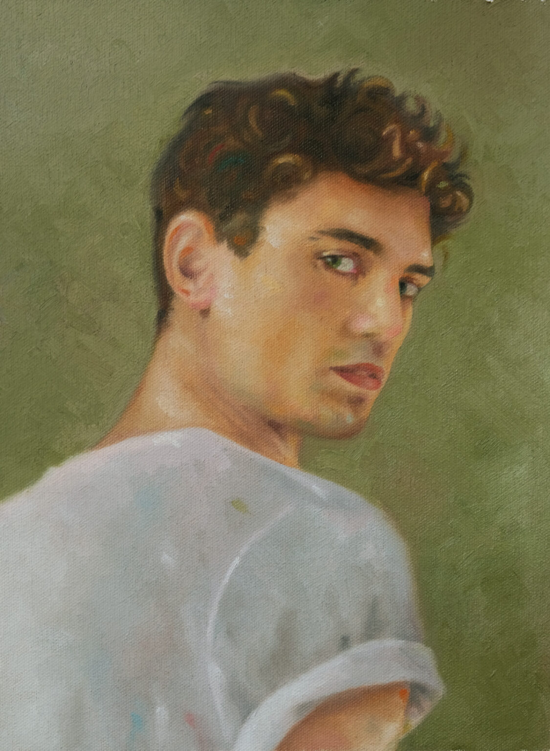 Young man turning over his shoulder in a light shirt against a muted green background.