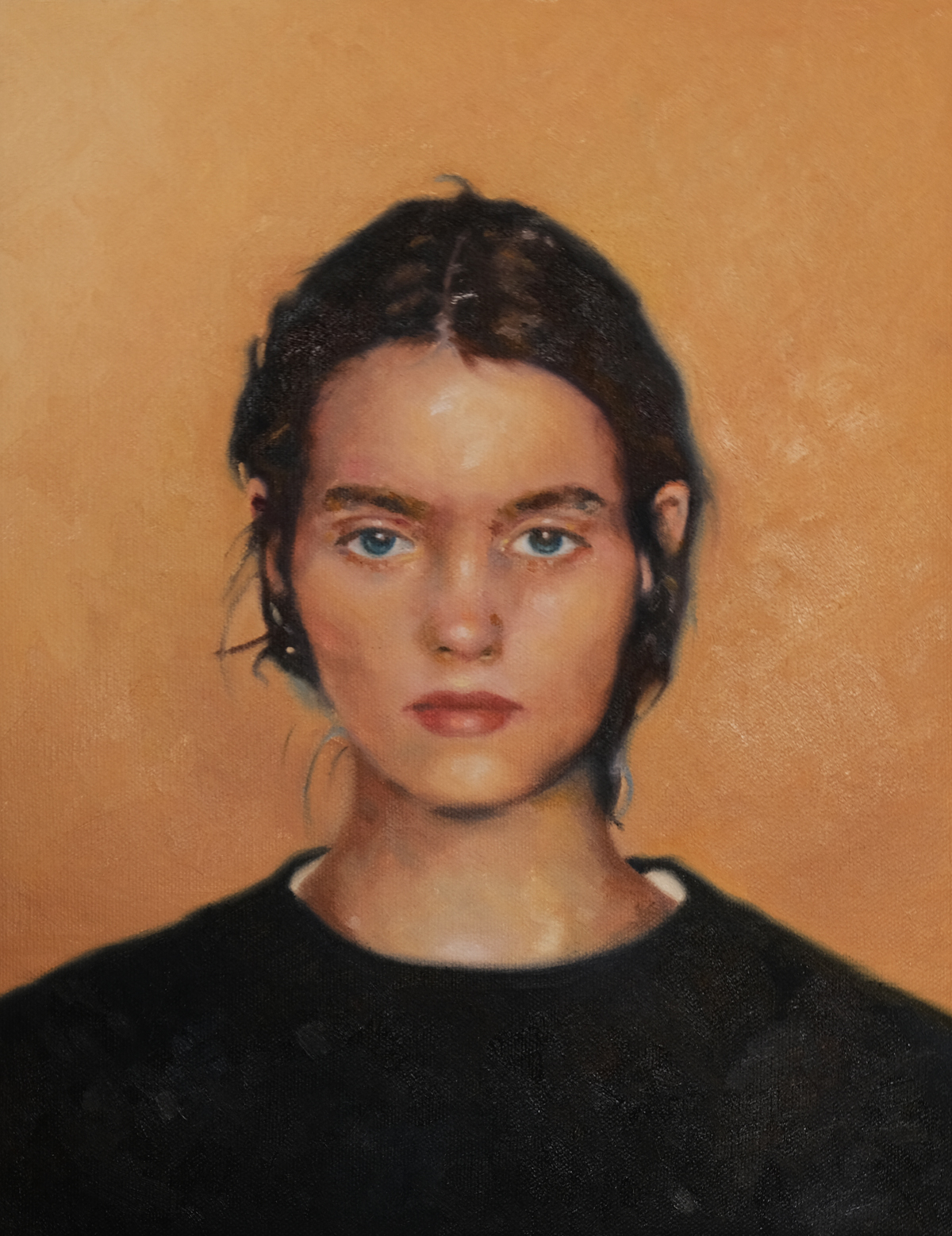 Frontal portrait of a dark-haired figure in a black top against a warm ochre background.